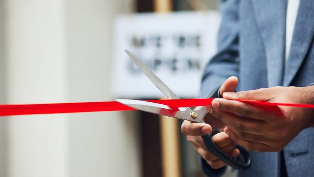 person cuts the red ribbon in front of a new business, featuring a sign saying we are open in the door